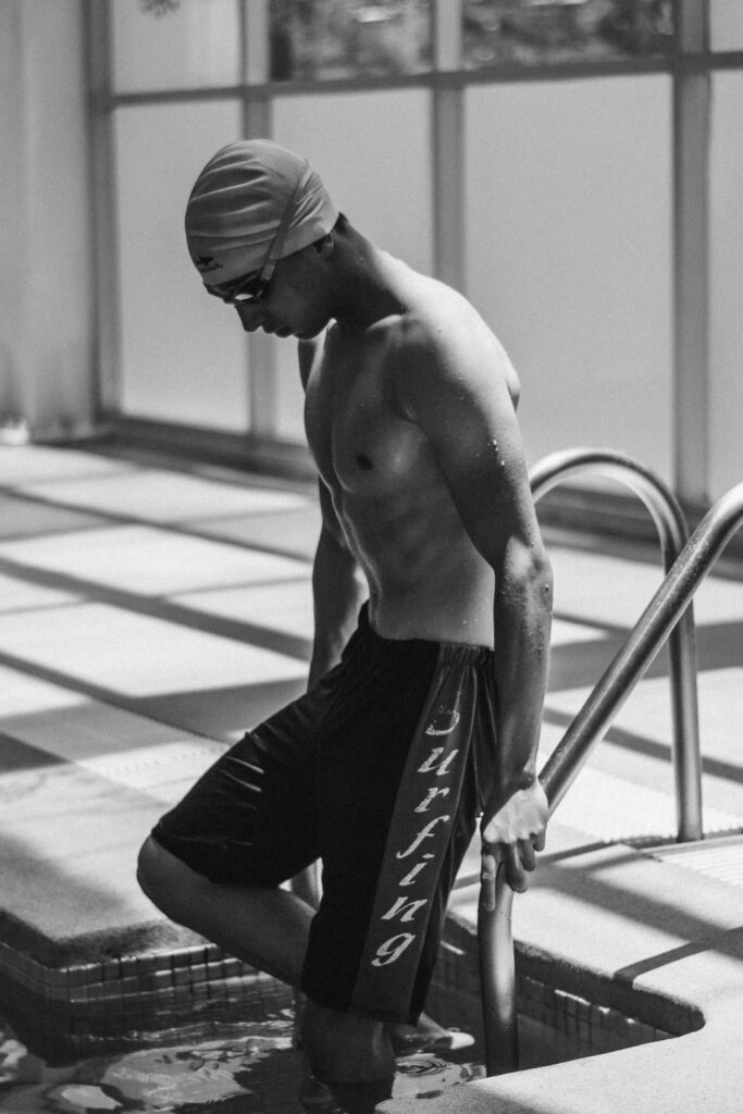 Black and white image of a male swimmer stepping into a pool, showcasing athletic physique and leisure.